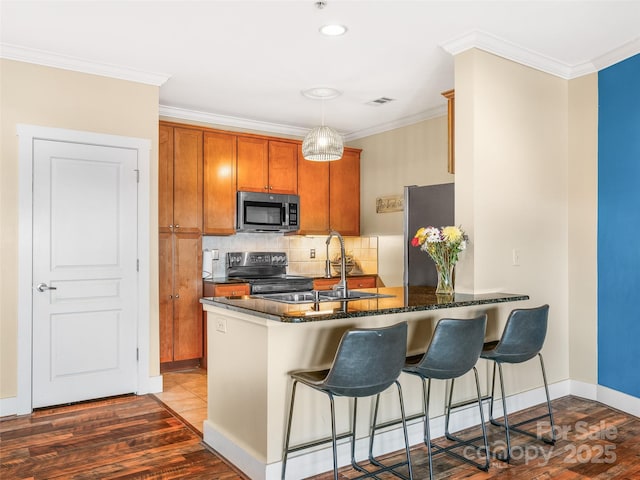 kitchen featuring brown cabinets, stainless steel appliances, ornamental molding, a sink, and a peninsula