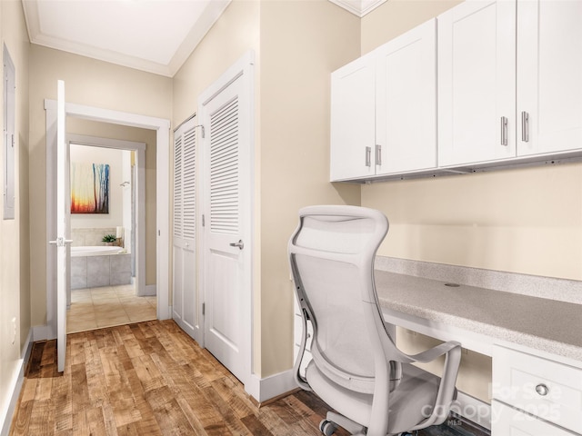 home office featuring baseboards, light wood-style flooring, ornamental molding, and built in desk