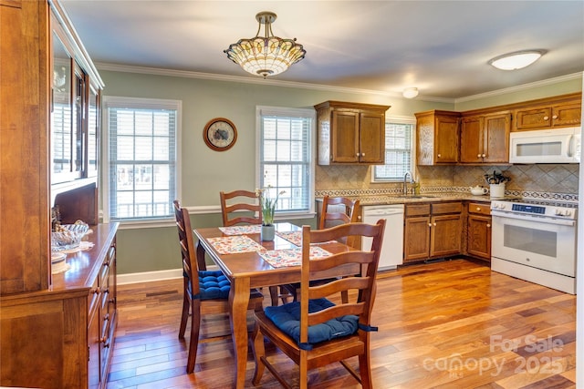 kitchen featuring white appliances, light hardwood / wood-style floors, crown molding, hanging light fixtures, and decorative backsplash