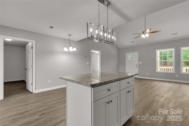 kitchen featuring lofted ceiling, wood-type flooring, light stone counters, a center island, and white cabinets