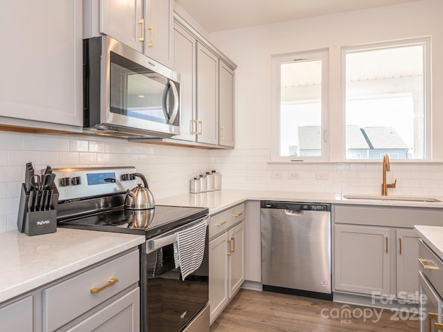 kitchen featuring stainless steel appliances, gray cabinets, light countertops, and a sink