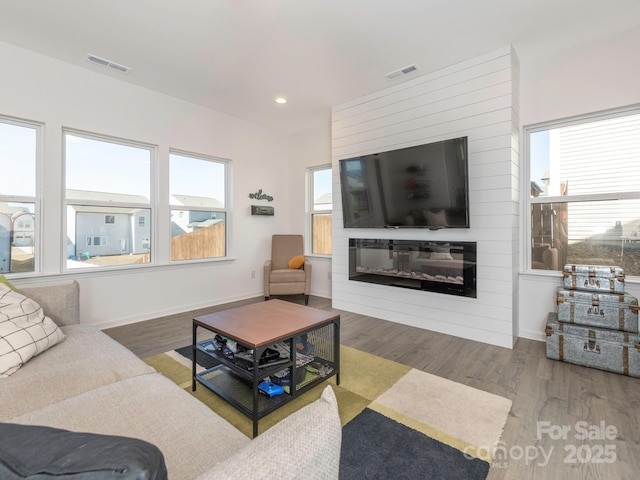 living room featuring a large fireplace, visible vents, and wood finished floors