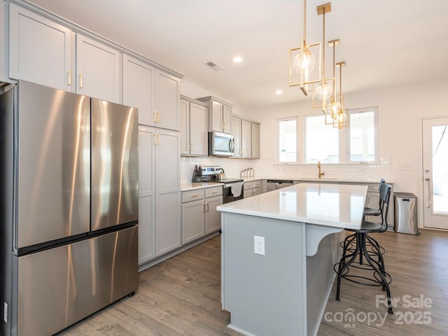 kitchen featuring visible vents, light countertops, appliances with stainless steel finishes, a center island, and tasteful backsplash