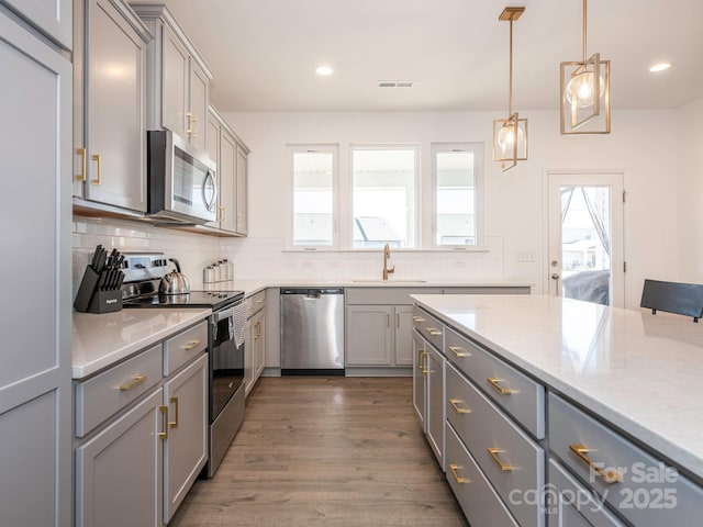 kitchen featuring decorative light fixtures, stainless steel appliances, light countertops, gray cabinetry, and a sink