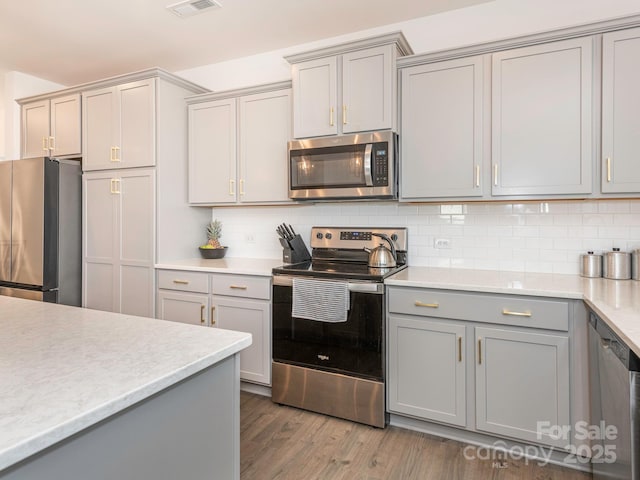 kitchen with decorative backsplash, stainless steel appliances, light countertops, and gray cabinetry