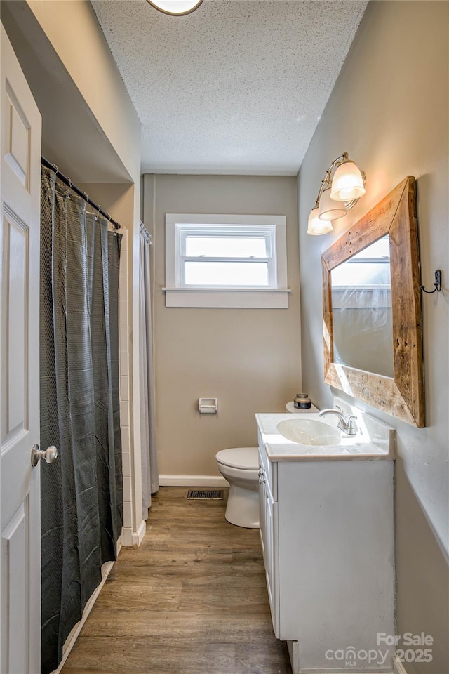 bathroom with toilet, wood-type flooring, a textured ceiling, vanity, and curtained shower