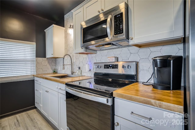 kitchen with sink, appliances with stainless steel finishes, butcher block counters, white cabinetry, and backsplash