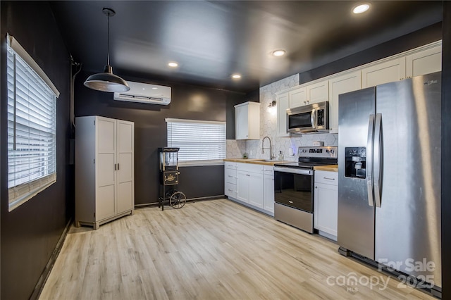 kitchen featuring appliances with stainless steel finishes, wood counters, white cabinetry, hanging light fixtures, and light hardwood / wood-style floors