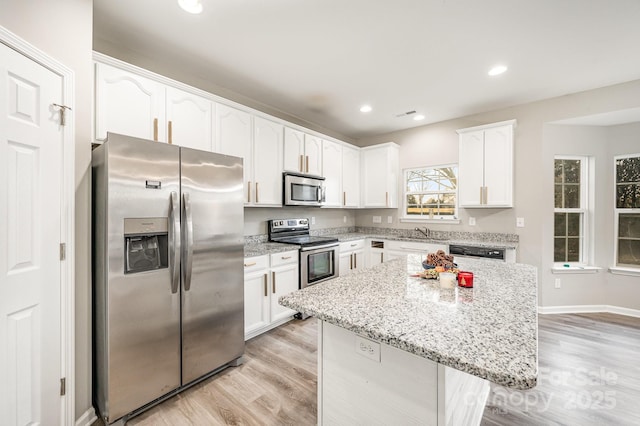 kitchen featuring appliances with stainless steel finishes, light wood finished floors, a center island, white cabinetry, and light stone countertops