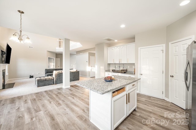 kitchen with freestanding refrigerator, open floor plan, hanging light fixtures, a center island, and white cabinetry