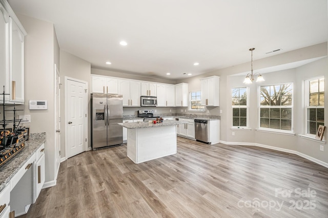 kitchen with appliances with stainless steel finishes, white cabinetry, light stone counters, pendant lighting, and a kitchen island