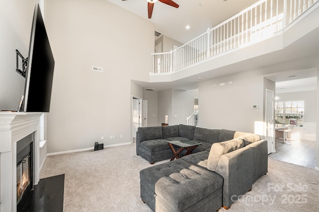 living area featuring ceiling fan, baseboards, visible vents, light carpet, and a glass covered fireplace