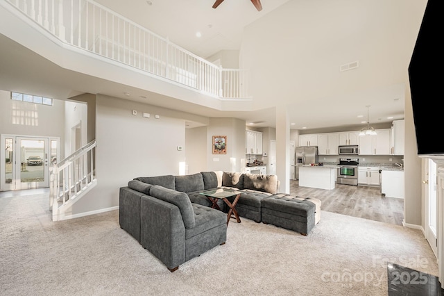 living area featuring a towering ceiling, visible vents, baseboards, and stairway