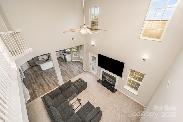 living area with wood finished floors, visible vents, a high ceiling, a fireplace with flush hearth, and ceiling fan