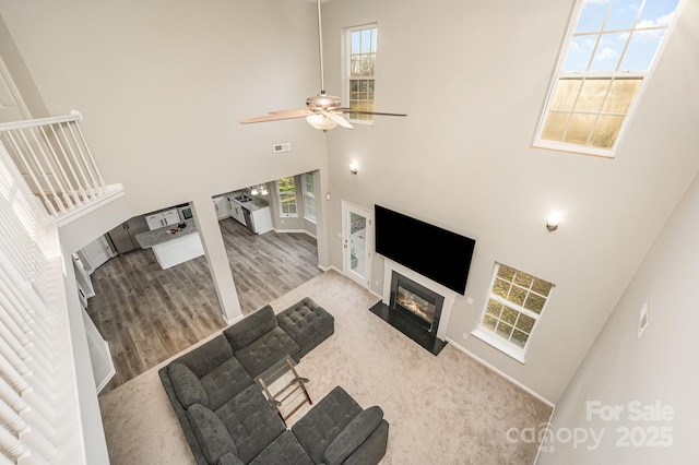 living room featuring a ceiling fan, wood finished floors, visible vents, a high ceiling, and a fireplace with flush hearth