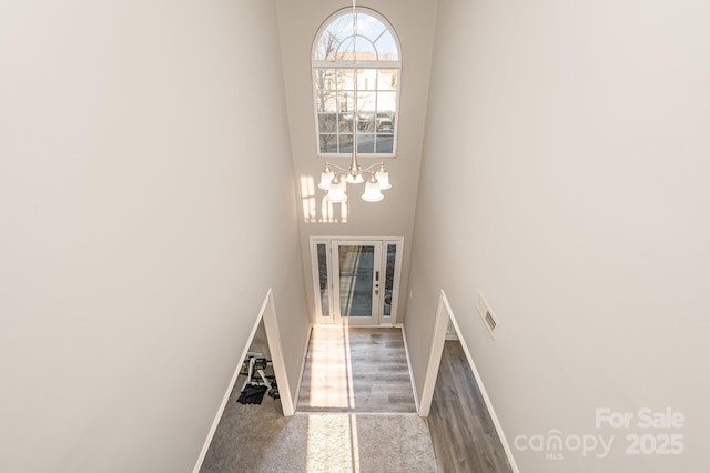 stairway featuring a towering ceiling, wood finished floors, visible vents, baseboards, and a chandelier