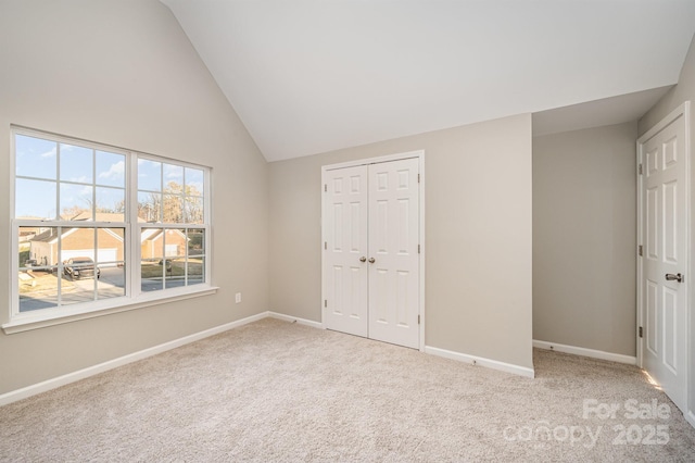 unfurnished bedroom with baseboards, a closet, high vaulted ceiling, and light colored carpet