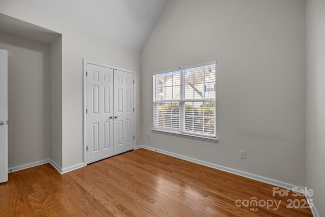 unfurnished bedroom featuring lofted ceiling, a closet, light wood-style flooring, and baseboards