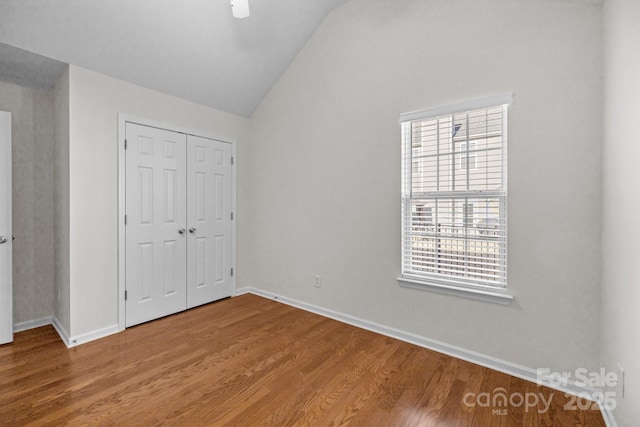 unfurnished bedroom with vaulted ceiling, a closet, wood finished floors, and baseboards