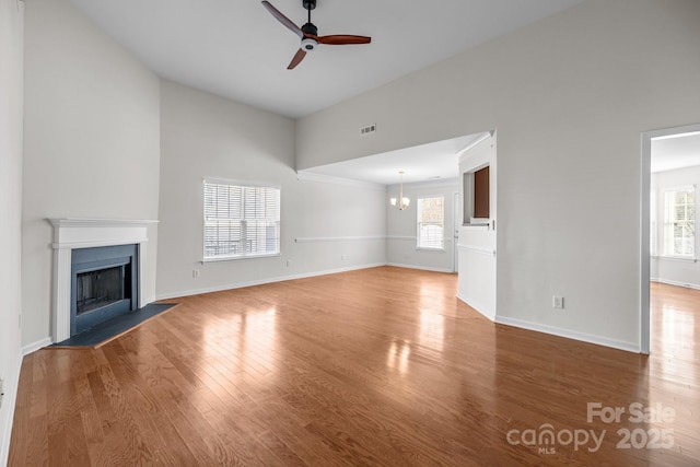 unfurnished living room featuring ceiling fan with notable chandelier, a healthy amount of sunlight, a fireplace, and wood finished floors