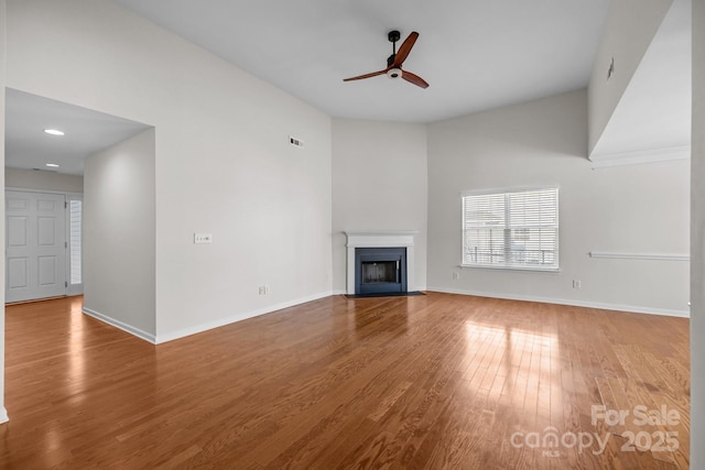 unfurnished living room featuring wood finished floors, a fireplace with flush hearth, a ceiling fan, and baseboards