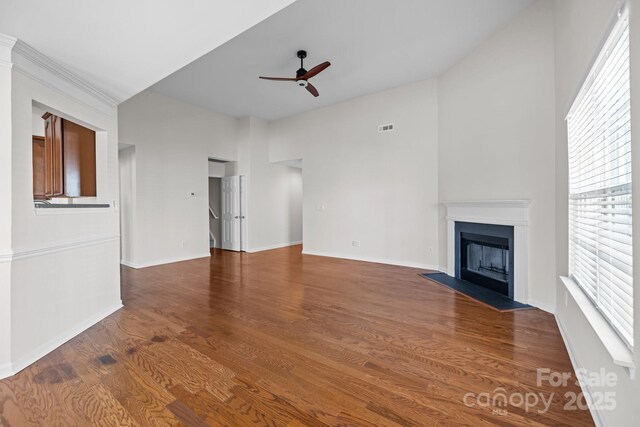 unfurnished living room featuring baseboards, visible vents, a ceiling fan, a fireplace with flush hearth, and dark wood-style flooring