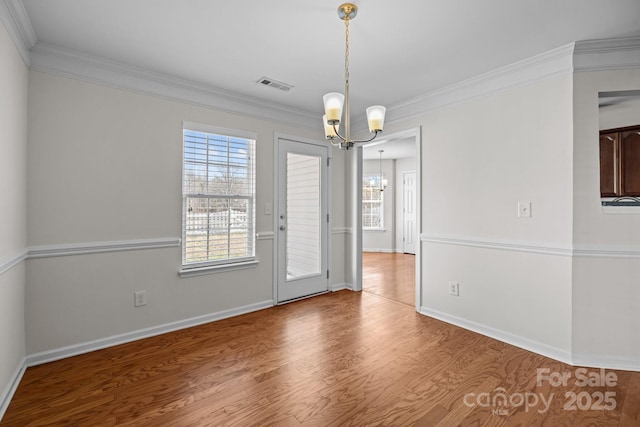 spare room featuring a notable chandelier, visible vents, ornamental molding, wood finished floors, and baseboards