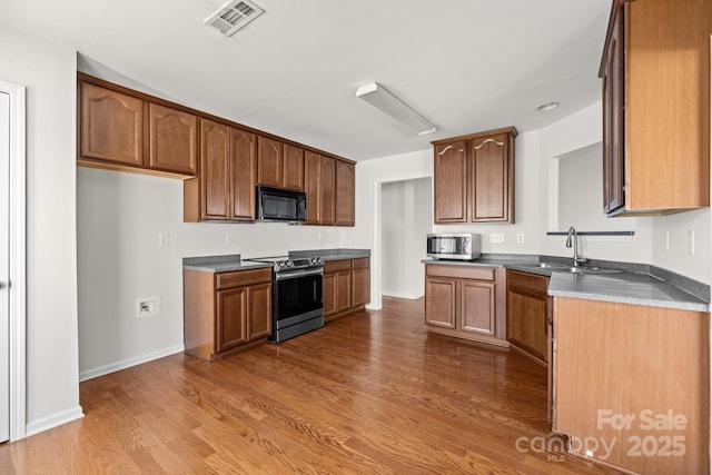 kitchen featuring black microwave, visible vents, brown cabinets, dark countertops, and stainless steel range with electric stovetop