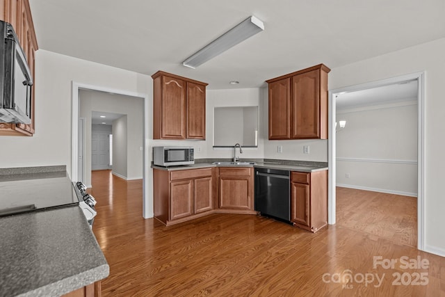 kitchen with black dishwasher, dark countertops, stainless steel microwave, a sink, and wood finished floors