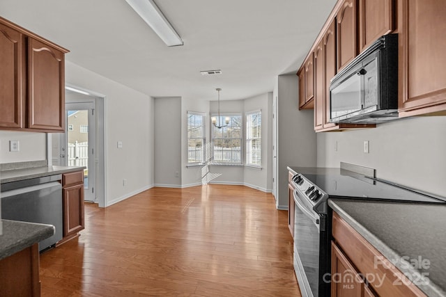 kitchen featuring hanging light fixtures, appliances with stainless steel finishes, dark countertops, and brown cabinets