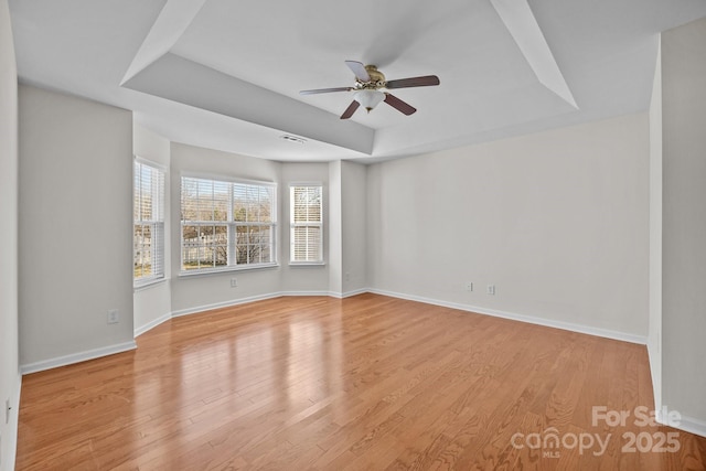 empty room with light wood finished floors, visible vents, baseboards, and a raised ceiling