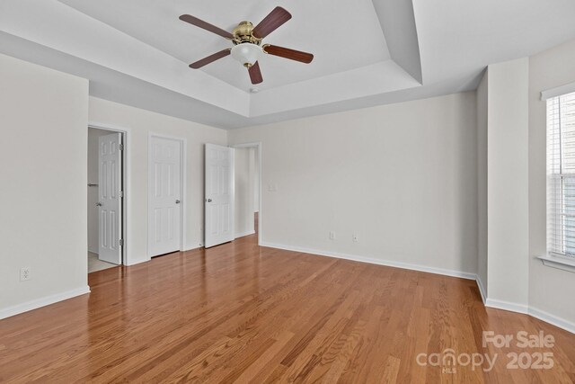 unfurnished bedroom featuring wood finished floors, a raised ceiling, and baseboards