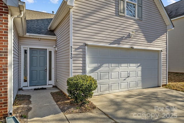 entrance to property with a garage, driveway, roof with shingles, and brick siding