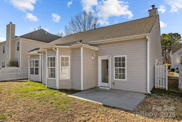 rear view of property featuring roof with shingles, a chimney, a lawn, a patio area, and fence