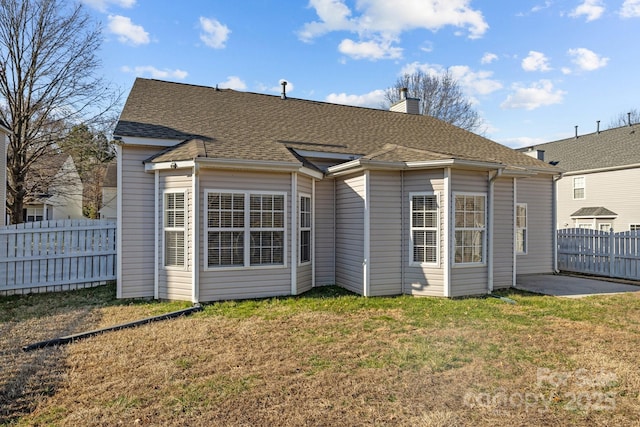 back of house featuring a shingled roof, fence, a chimney, and a lawn