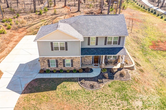 view of front of house with a front yard, stone siding, roof with shingles, and covered porch