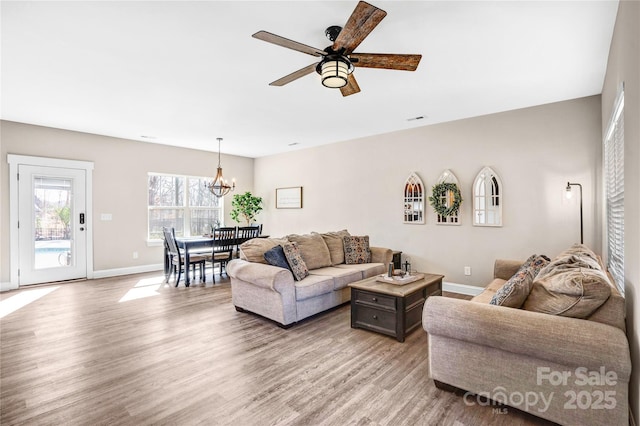 living area with light wood-type flooring, visible vents, baseboards, and ceiling fan with notable chandelier