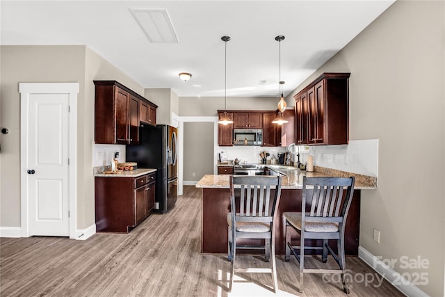 kitchen with a peninsula, light wood finished floors, appliances with stainless steel finishes, and light stone counters