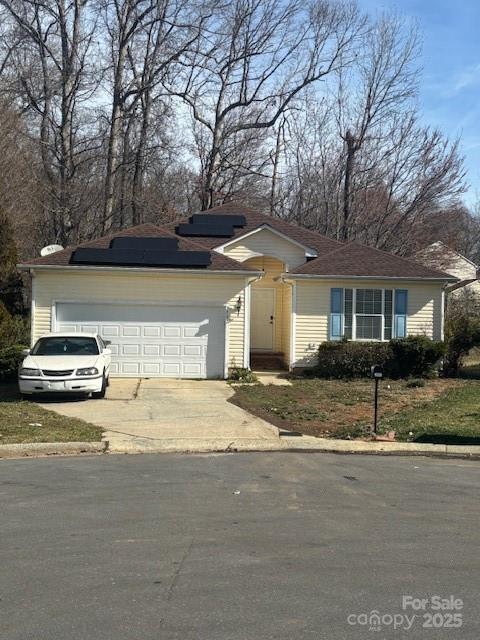 single story home featuring an attached garage, driveway, and roof mounted solar panels