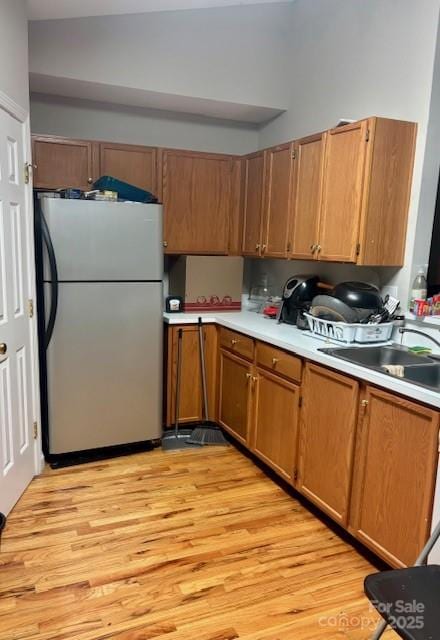 kitchen featuring a sink, light wood-style floors, light countertops, freestanding refrigerator, and brown cabinetry