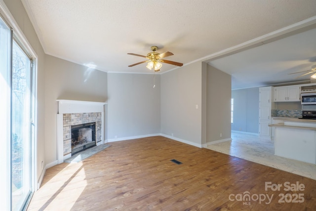 unfurnished living room featuring a stone fireplace, ornamental molding, ceiling fan, and light hardwood / wood-style flooring