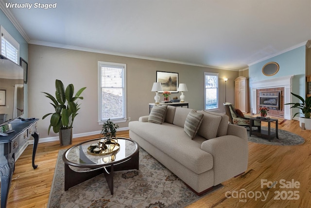 living area featuring crown molding, a fireplace, light wood-type flooring, and baseboards