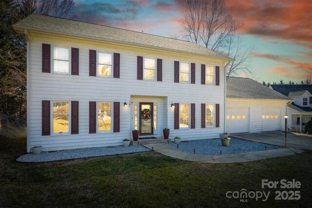 colonial-style house with a front lawn, roof with shingles, concrete driveway, and an attached garage