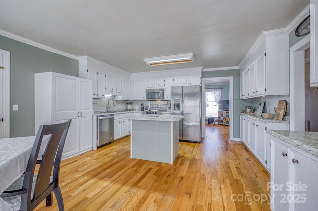 kitchen featuring a kitchen island, ornamental molding, stainless steel appliances, white cabinets, and light wood-type flooring