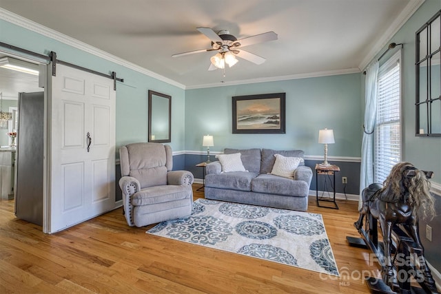 living area featuring wood finished floors, baseboards, ceiling fan, crown molding, and a barn door