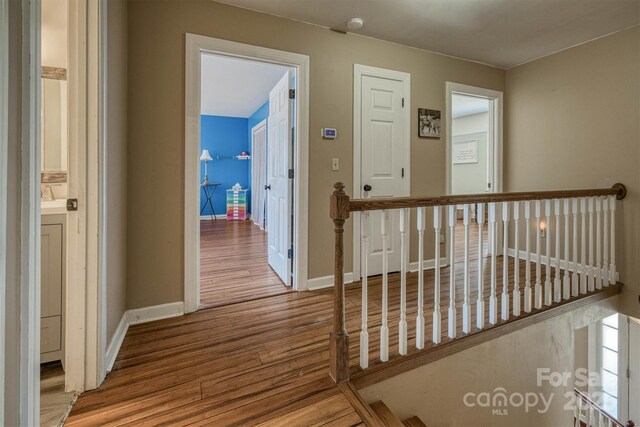 hall with an upstairs landing, wood finished floors, and baseboards