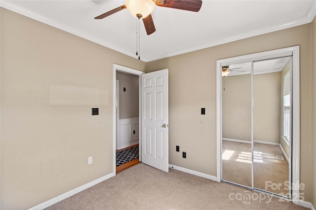 unfurnished bedroom featuring baseboards, a ceiling fan, light colored carpet, crown molding, and a closet