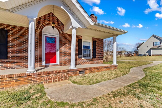 entrance to property with covered porch, a yard, brick siding, and a chimney