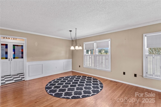 unfurnished dining area featuring a chandelier, ornamental molding, wood finished floors, and visible vents