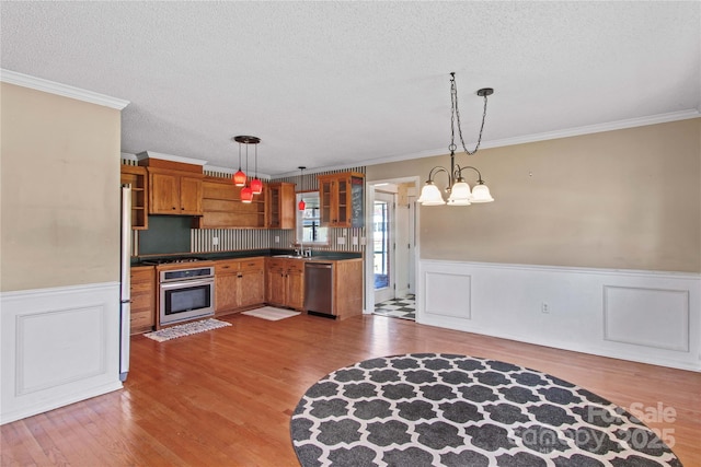 kitchen with a chandelier, a wainscoted wall, stainless steel appliances, wood finished floors, and brown cabinetry